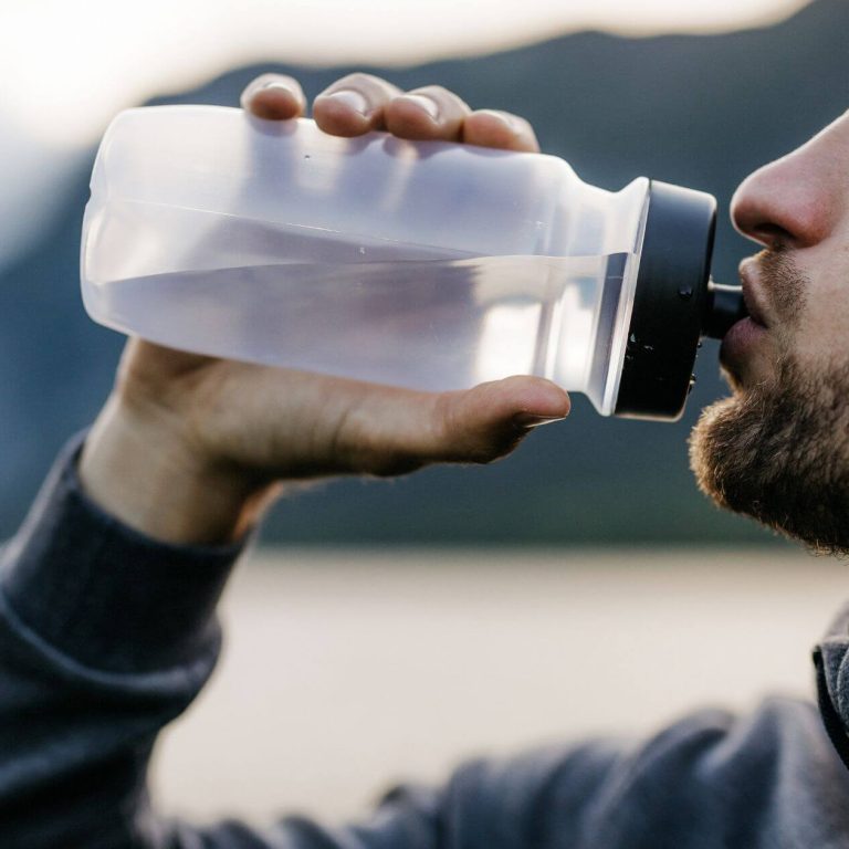 Man drinking water from a bottle outdoors.