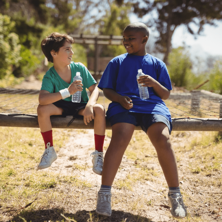 Two boys sitting on a bench in the grass.