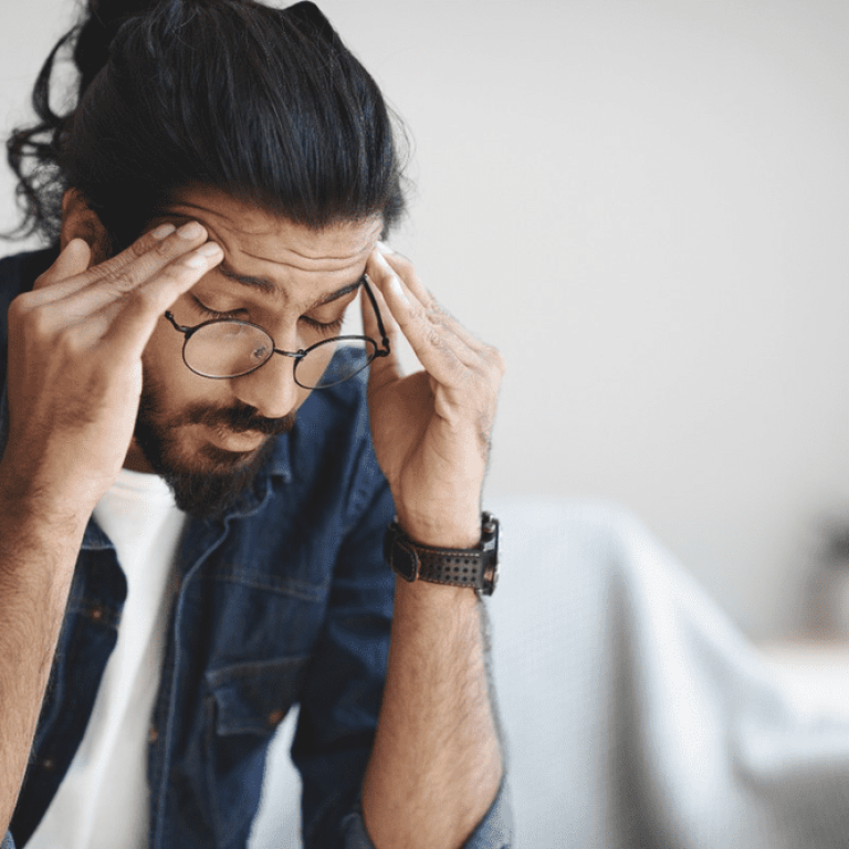A man with glasses is holding his head